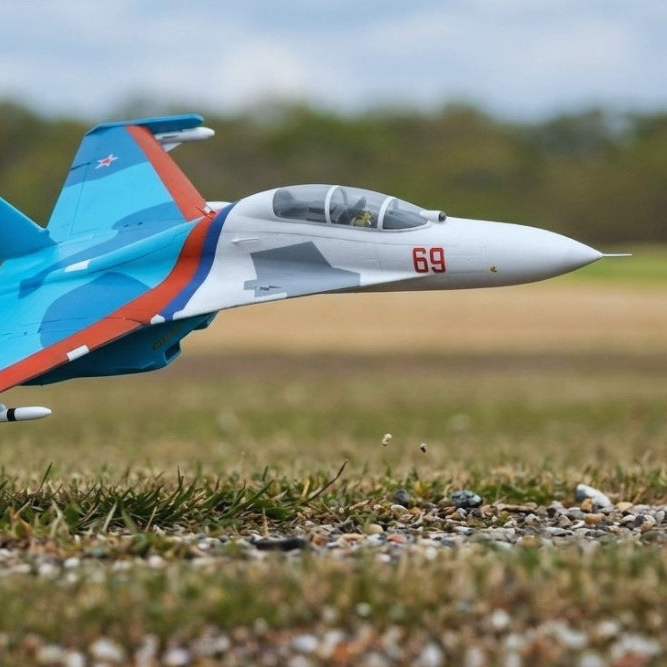 Model of a fighter jet on a grassy area with trees in the background